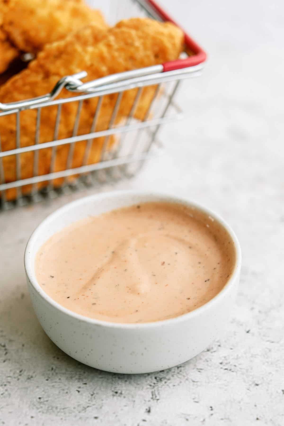 A bowl of Raising Cane’s Chicken Sauce with a basket of chicken tenders