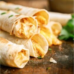 Slow Cooker Cheesy Chicken Taquitos stacked so you can see the inside of the taquitos on a wooden surface.
