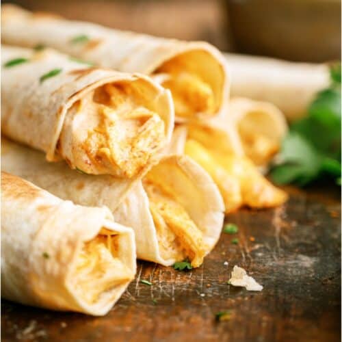 Slow Cooker Cheesy Chicken Taquitos stacked so you can see the inside of the taquitos on a wooden surface.