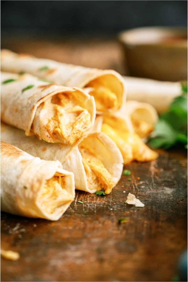 Slow Cooker Cheesy Chicken Taquitos stacked so you can see the inside of the taquitos on a wooden surface.