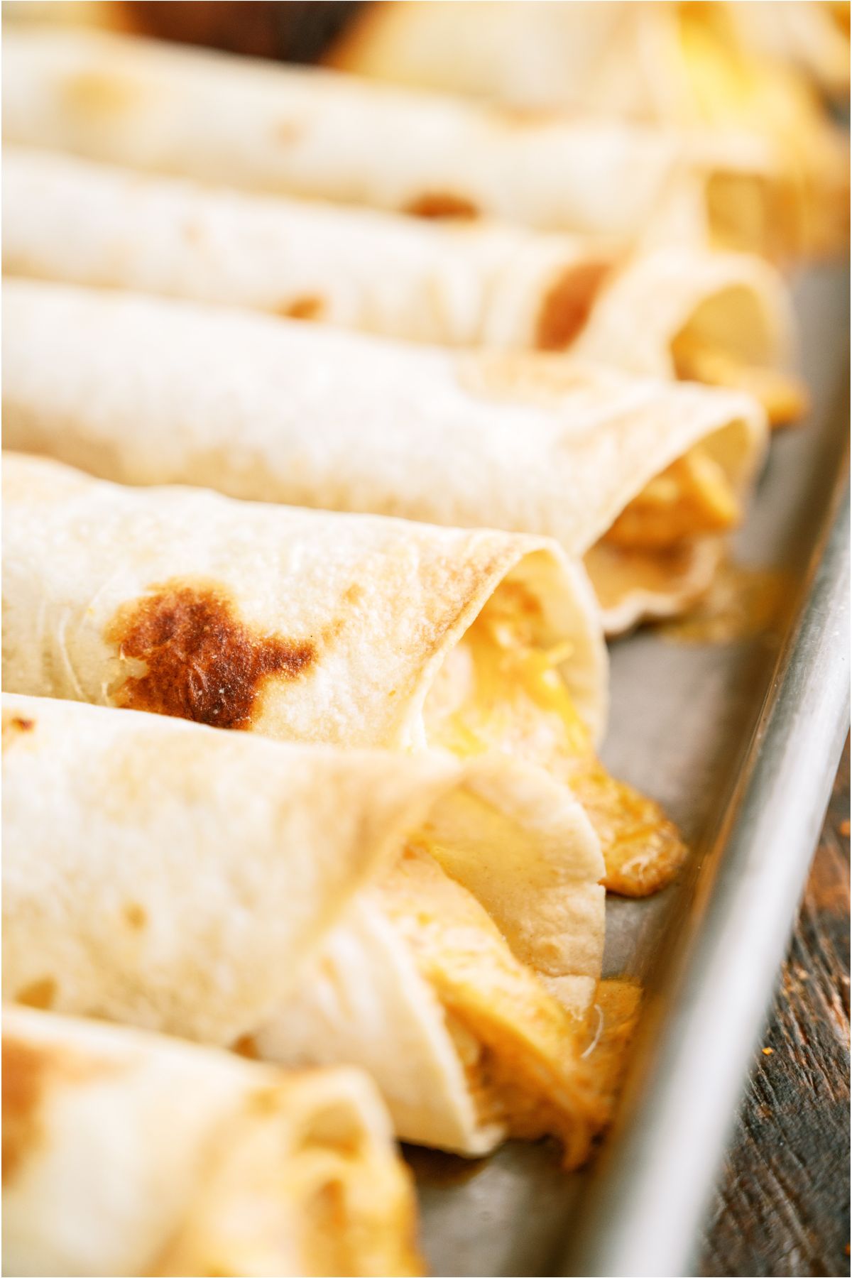 Close up of Slow Cooker Cheesy Chicken Taquitos on a baking sheet.