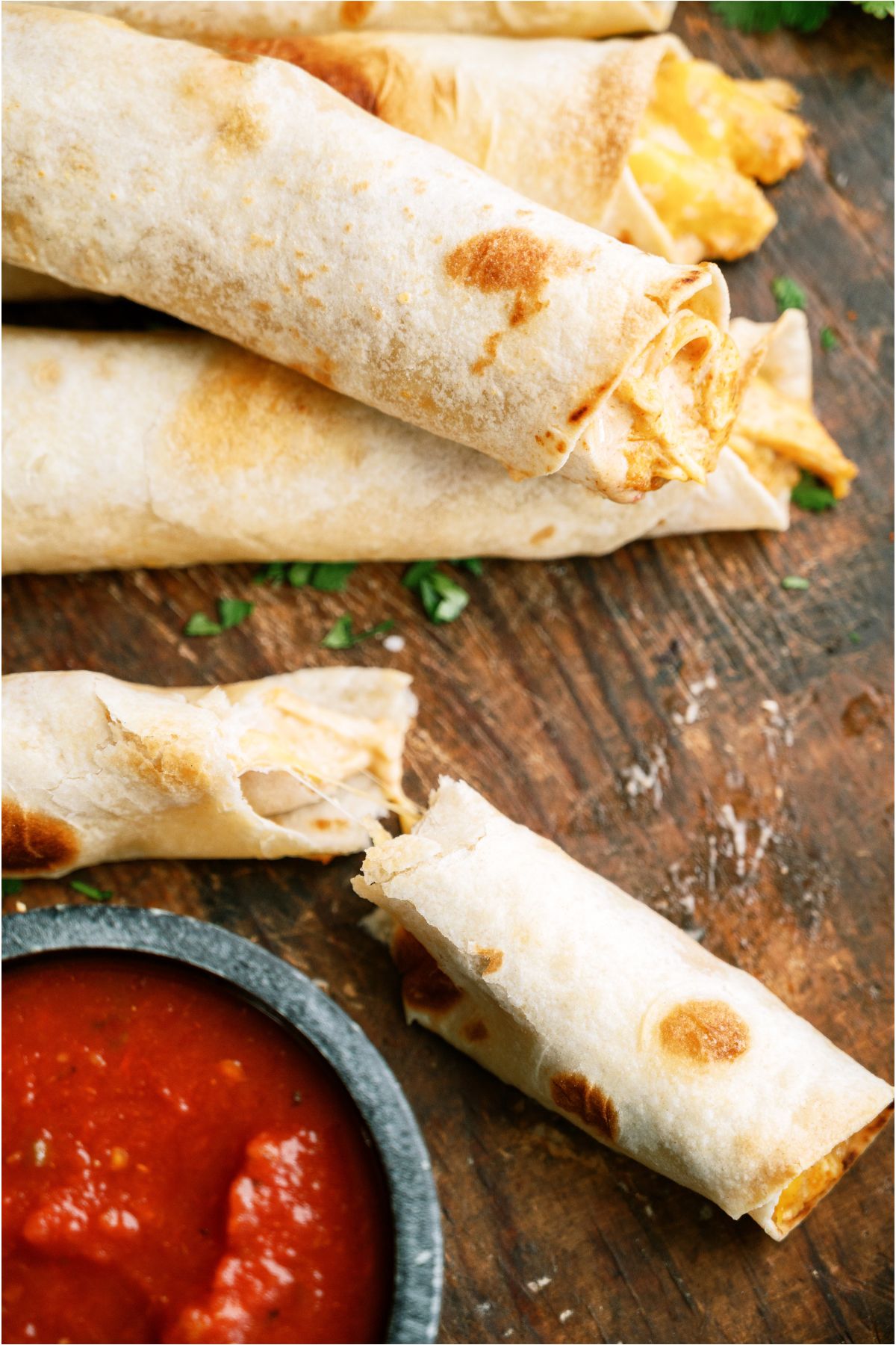 Several Slow Cooker Cheesy Chicken Taquitos with one broken in half and a small cup of dipping sauce.