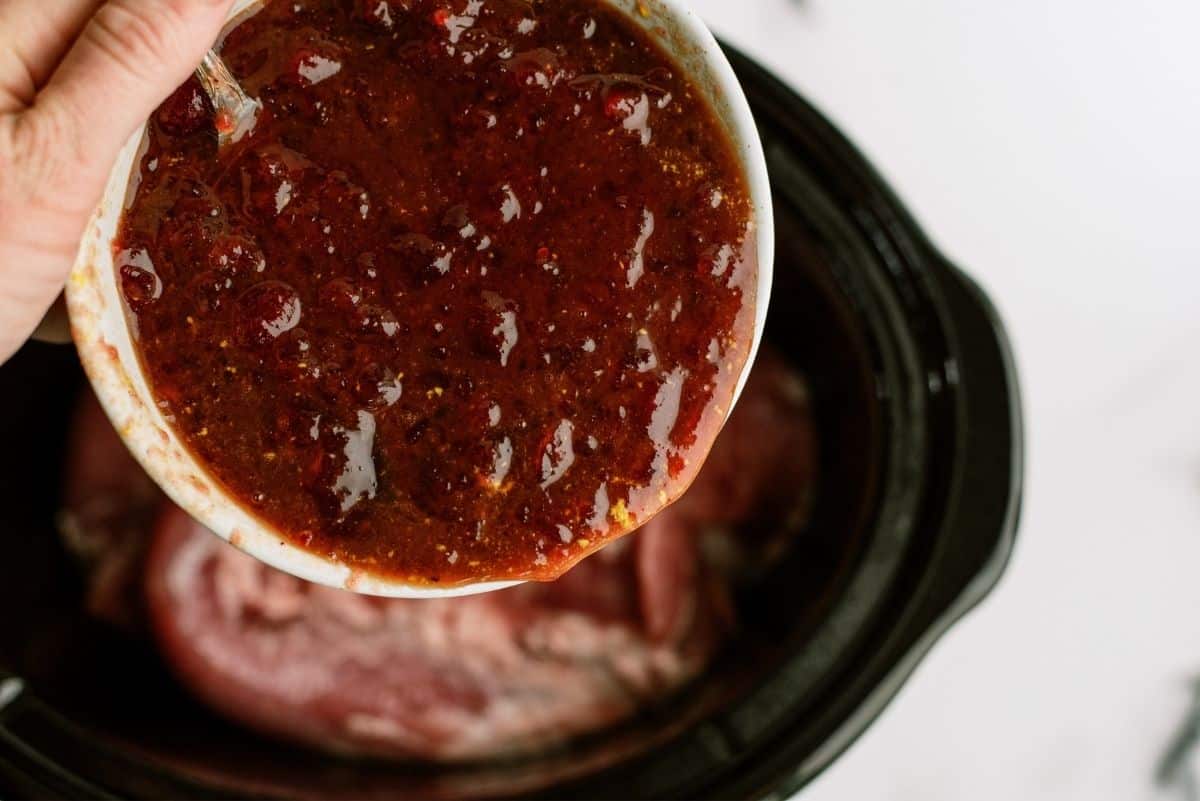 Cranberry sauce mixture being poured on top of pork in slow cooker