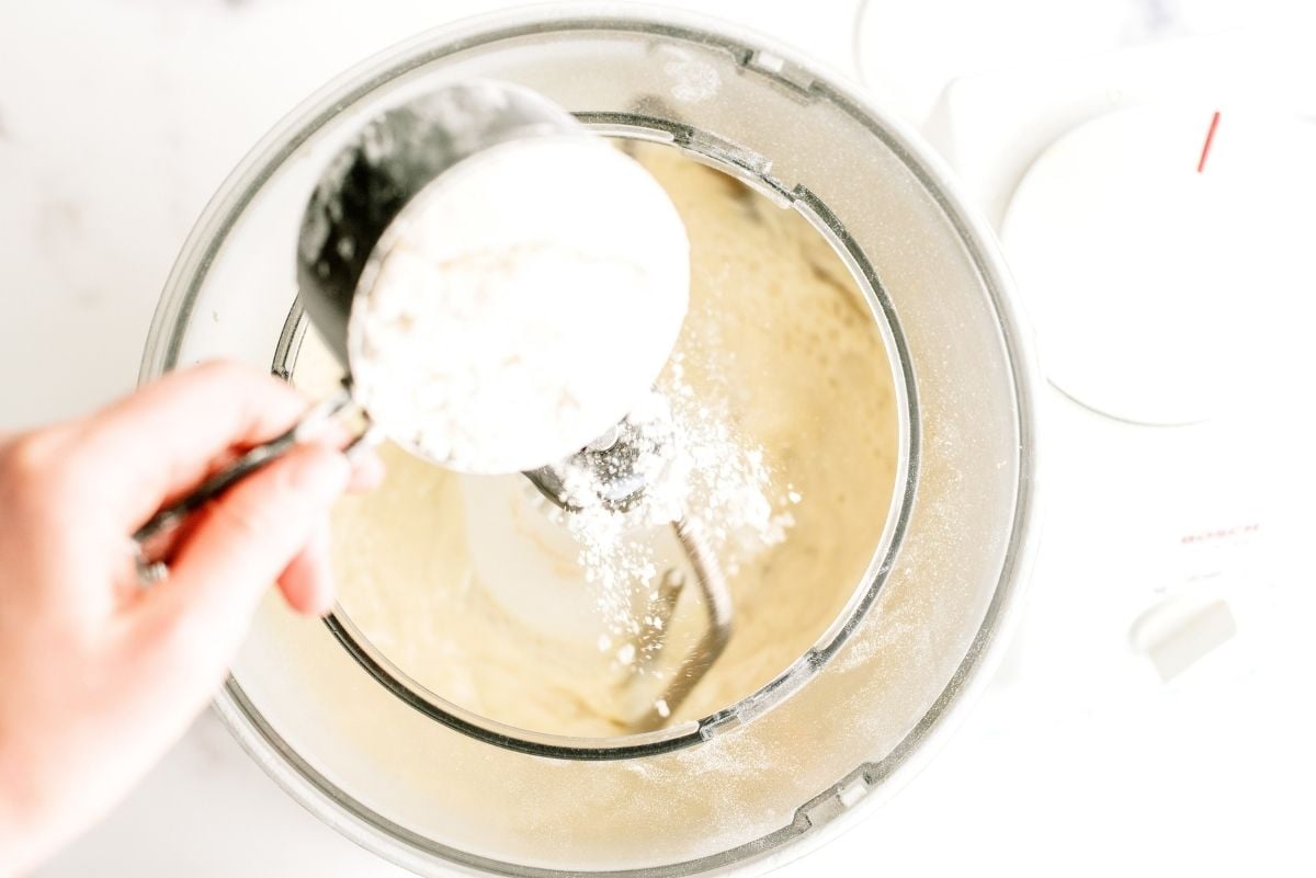 Pouring 1 cup of flour into the dough mixture inside the mixing bowl