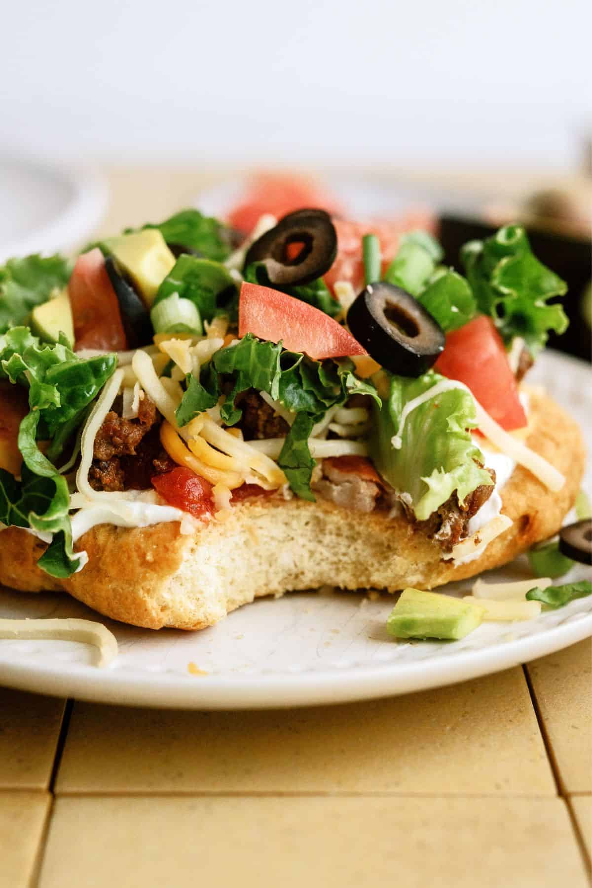 Air Fryer Indian Fry Bread Recipe (Navajo Tacos) on a plate with toppings and a bite missing