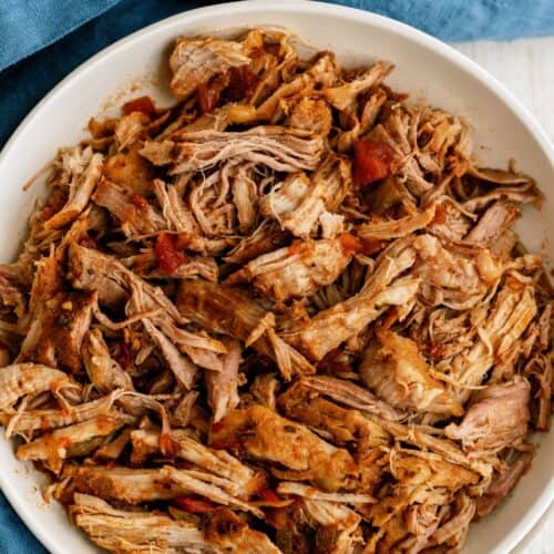 A white bowl filled with shredded cooked meat, seasoned with spices, placed on a blue cloth.