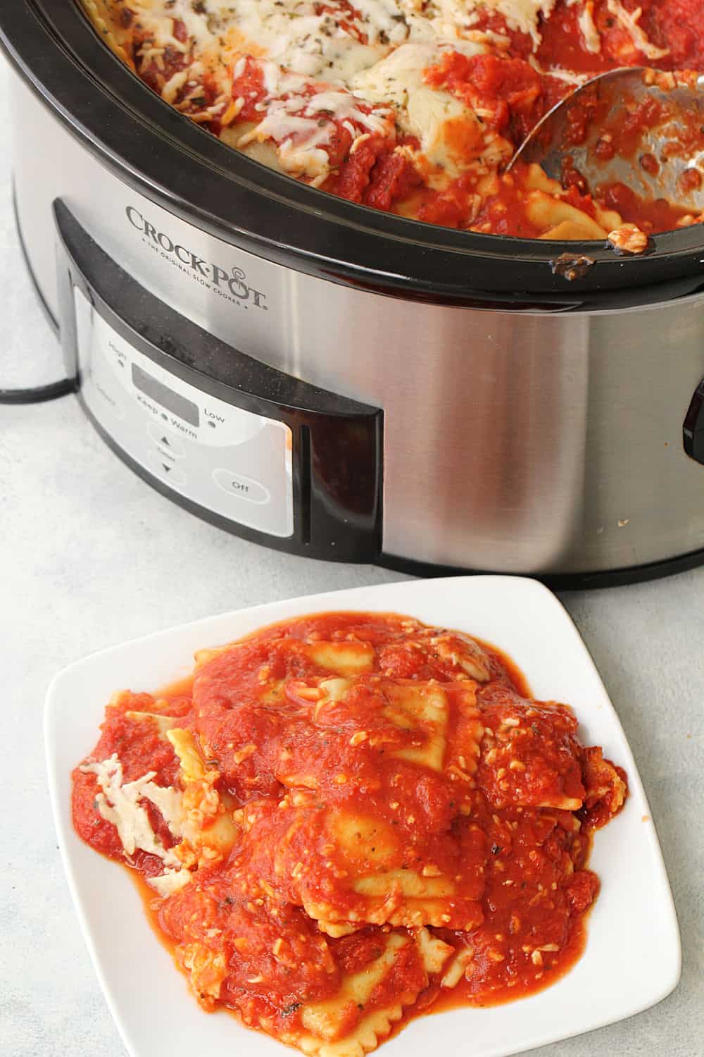 Crock Pot Cheesy Ravioli Casserole on a plate with the Crock Pot in the background