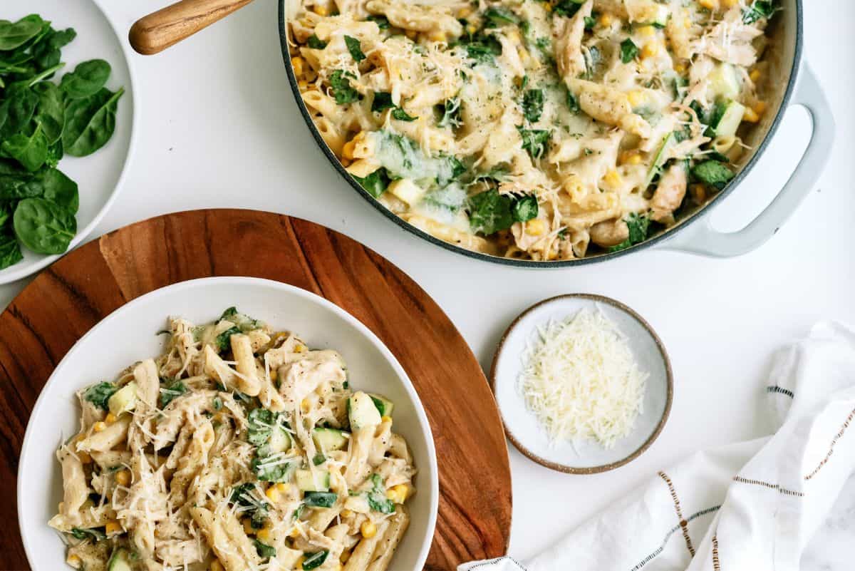 A serving of Chicken Pasta Casserole with Corn and Zucchini on a plate with a pan of Chicken Pasta Casserole with Corn and Zucchini in the background