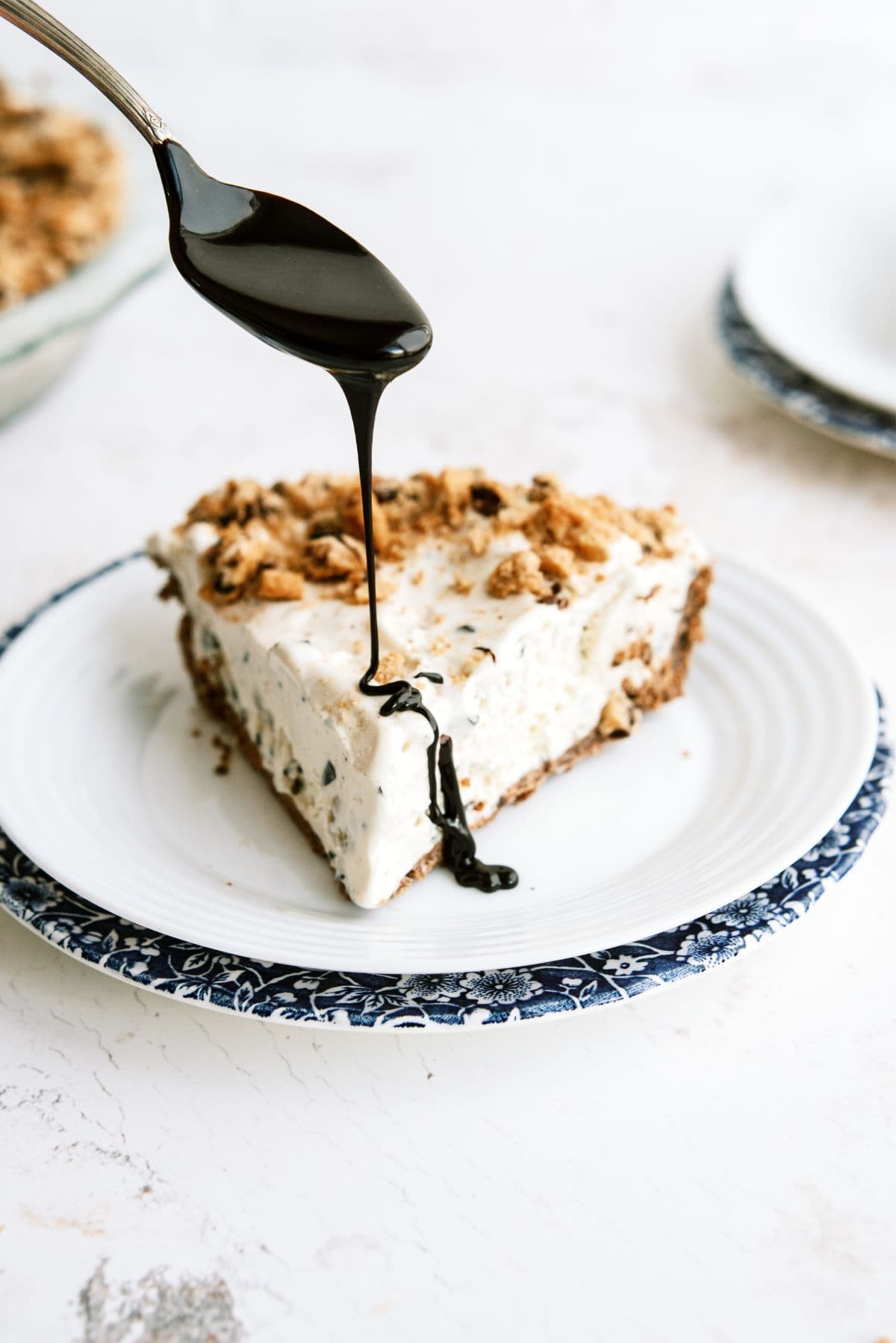 Drizzling fudge on top of a slice of Chocolate Chip Cookie Ice Cream Pie on a plate.
