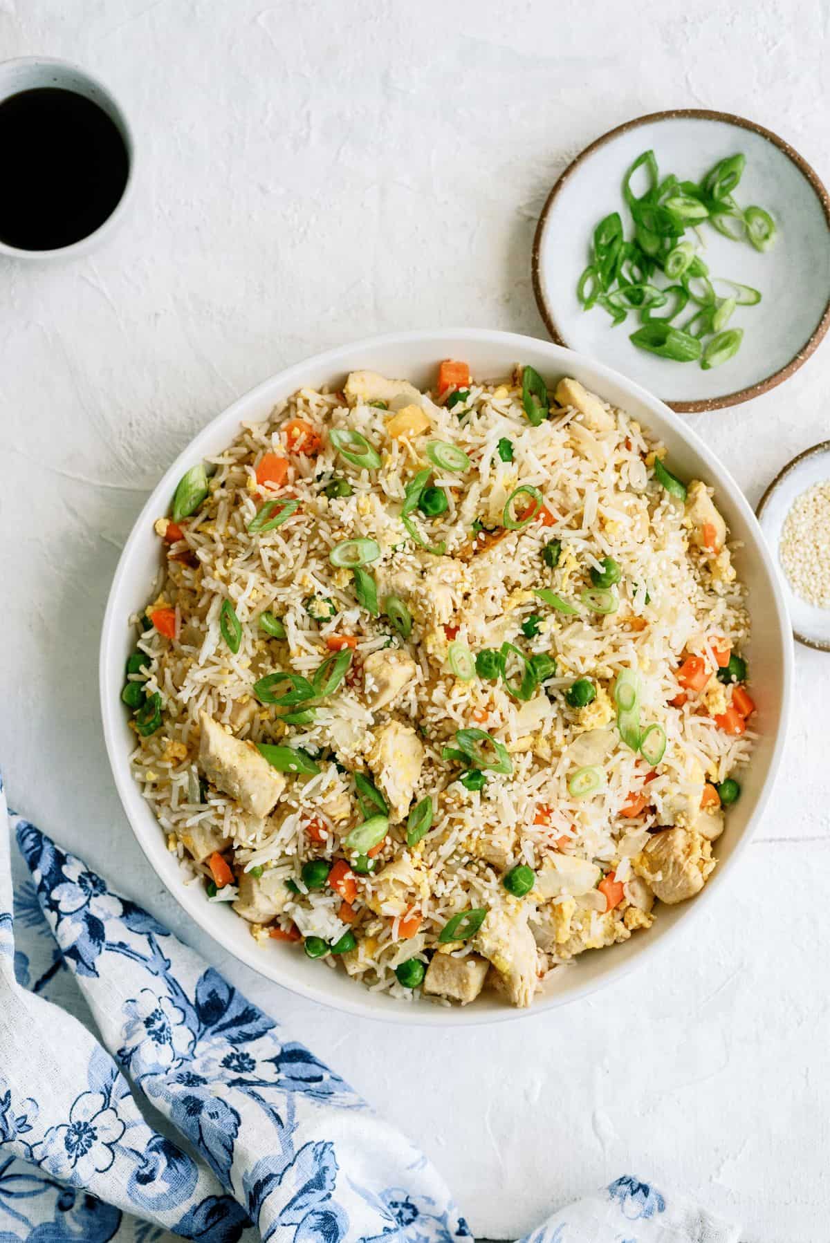 Top view of a white bowl filled with Instant Pot Chicken Fried Rice. Two small bowls on the side with soy sauce and sliced green onions.