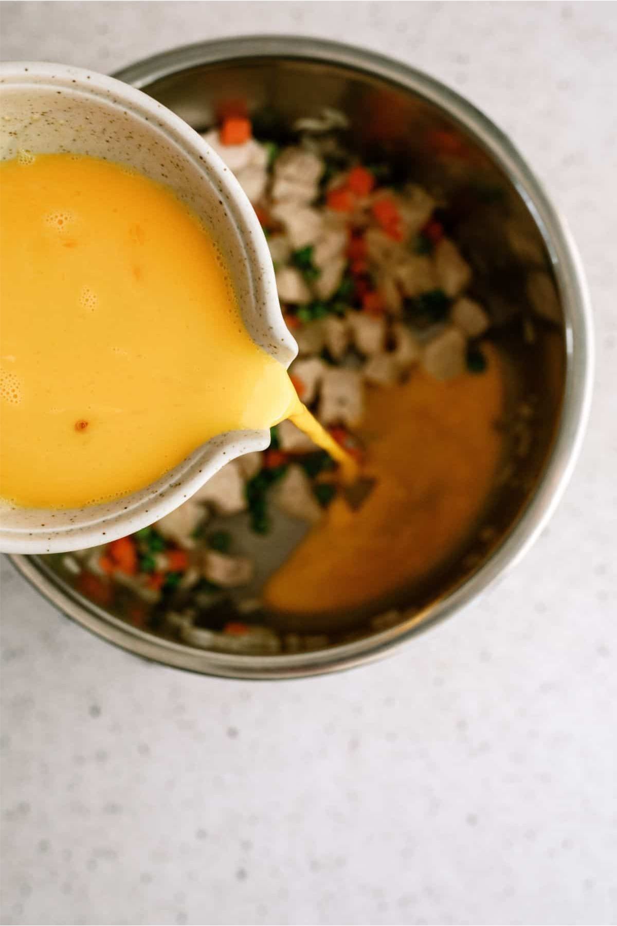 Pouring egg mixture from a measuring cup into the Instant Pot with chicken and mixed veggies.