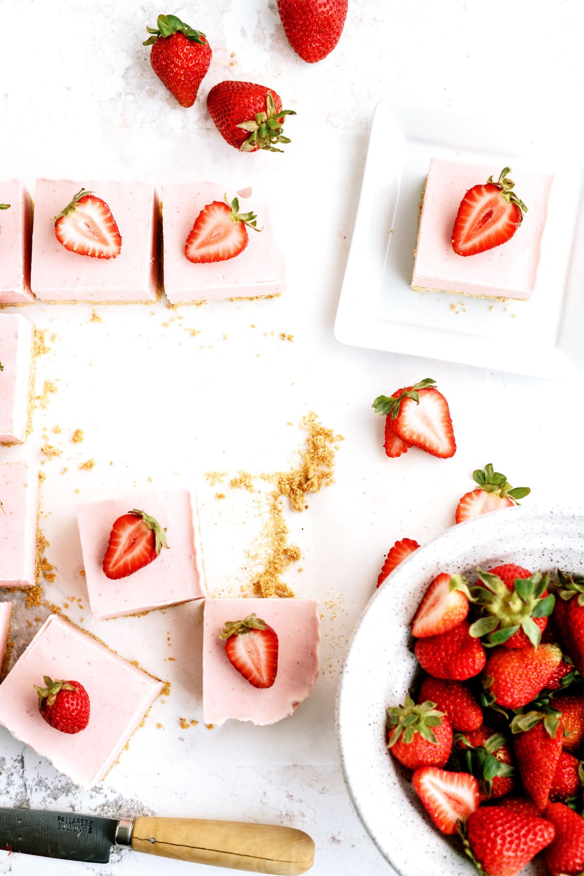 Top view of No Bake Strawberry Cheesecake Bars cut into squares with a bowl of fresh strawberries