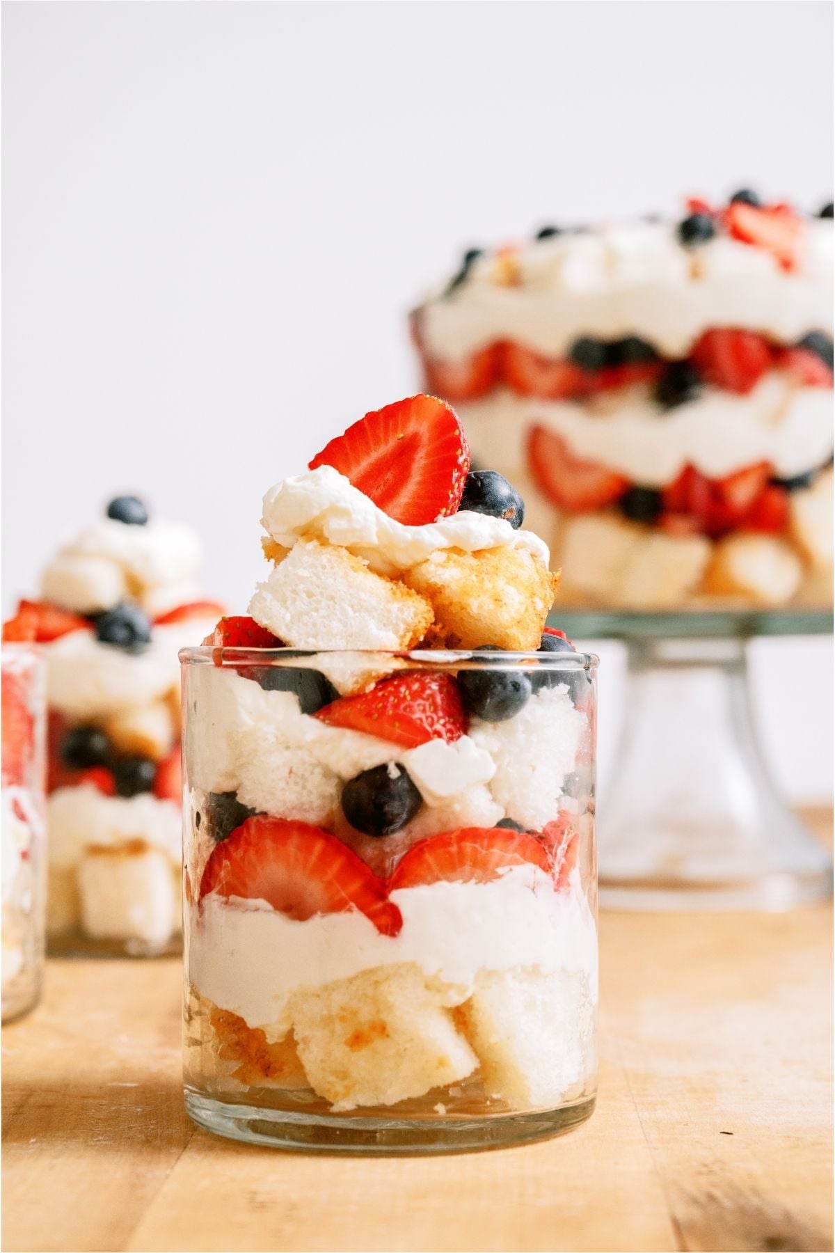 Patriotic Berry Trifle in a cup with a larger Patriotic Berry Trifle in a trifle dish in the background.