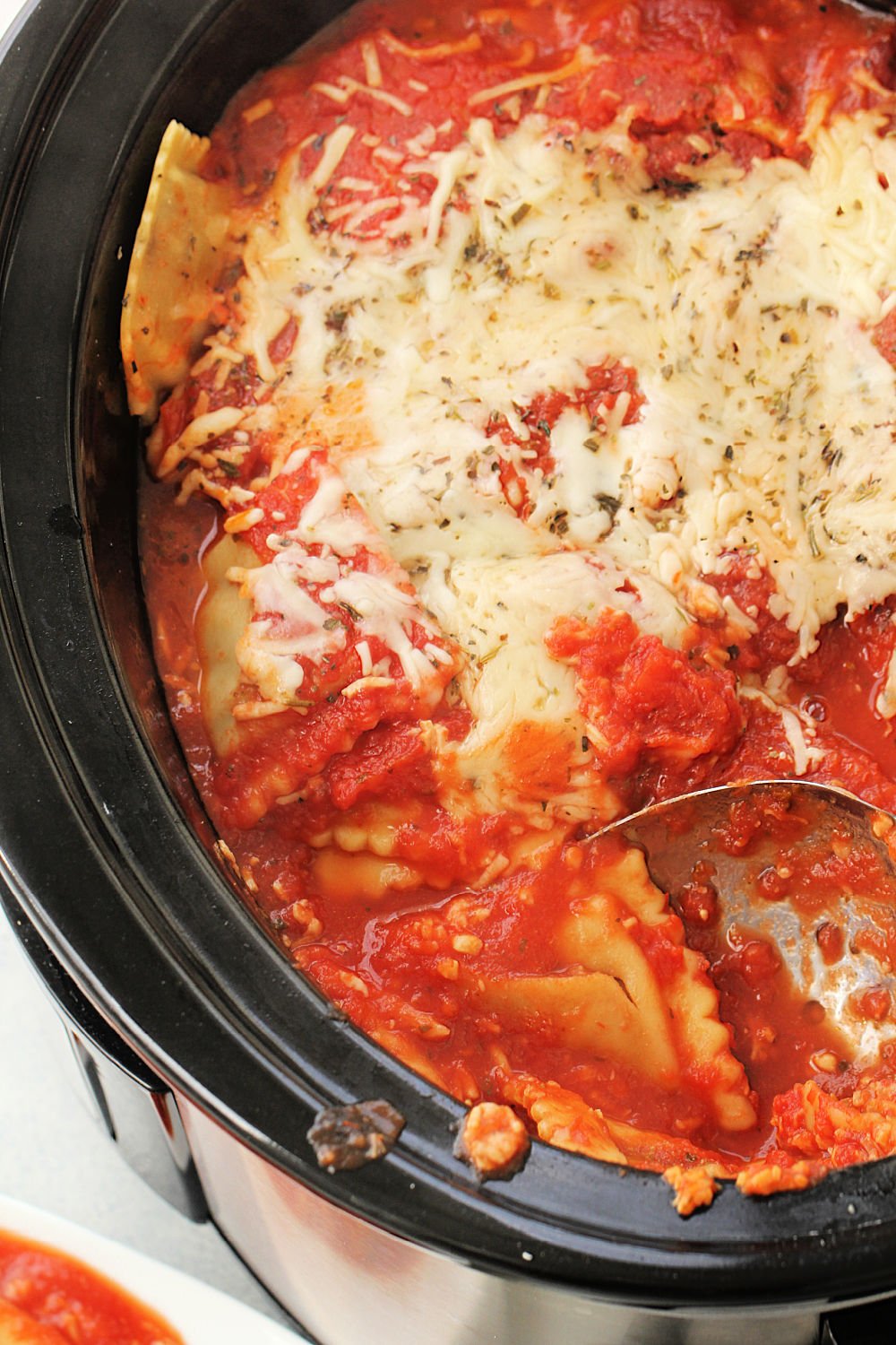 Crock Pot Cheesy Ravioli Casserole in the Slow Cooker with a serving spoon