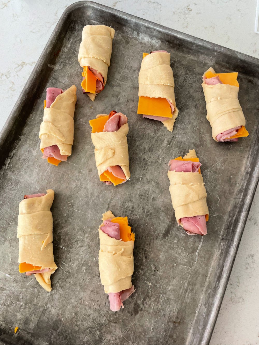 Ham and Cheese Crescents rolled up on sheet pan ready to bake