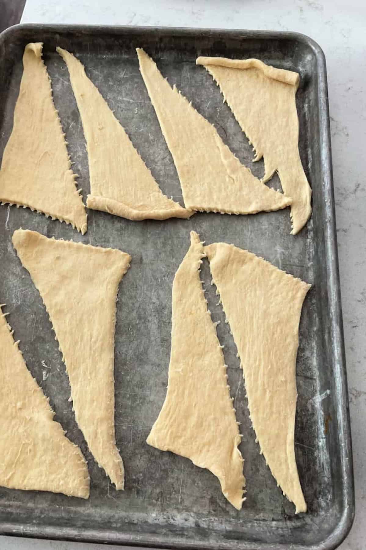 Unbaked crescent rolls on a baking sheet, each topped with a slice of ham and cheddar cheese.