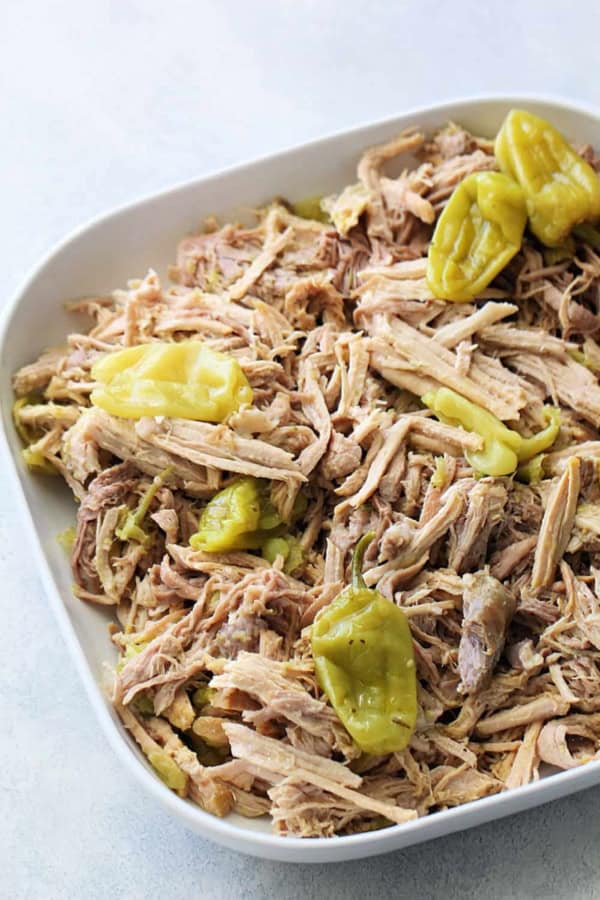 Shredded cooked pork topped with several whole pepperoncini peppers served in a white dish.
