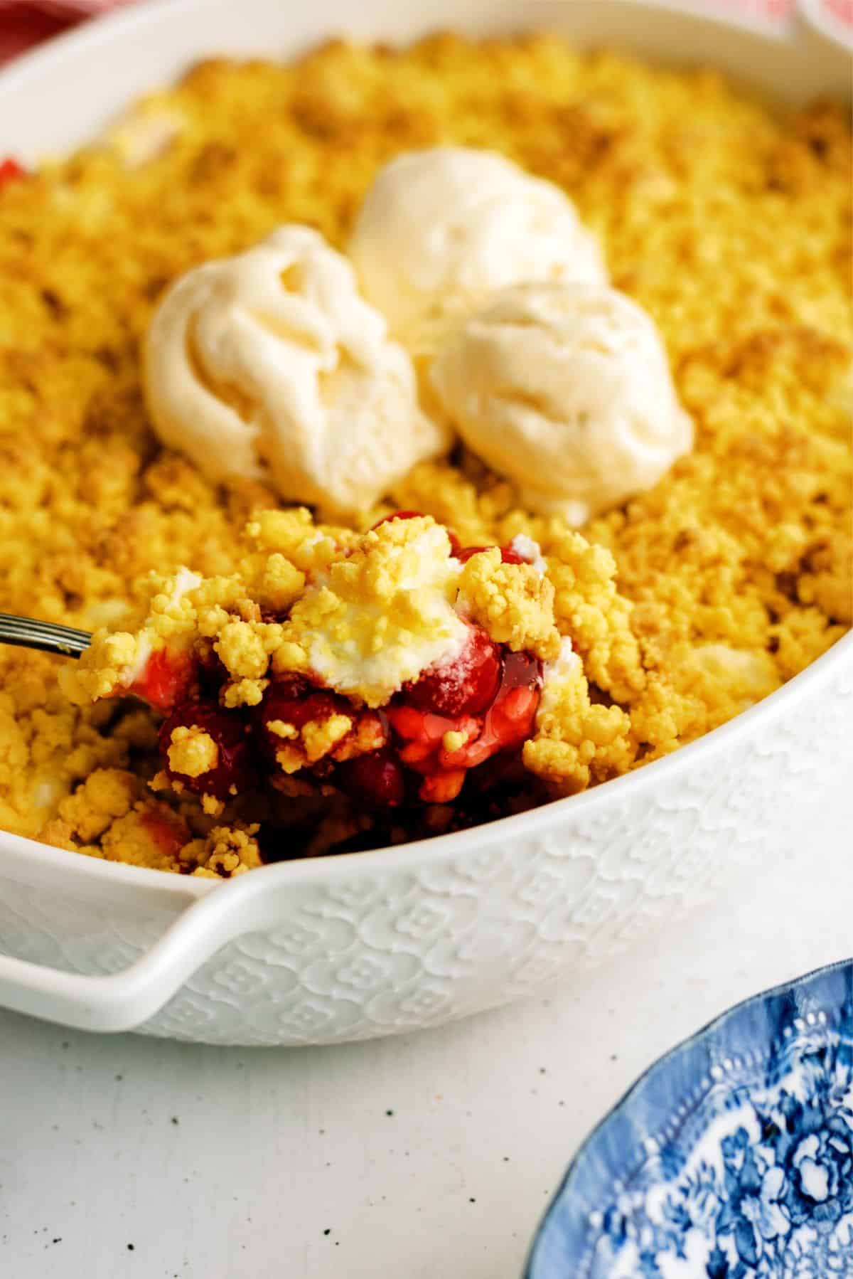 Cherry Cheesecake Dump Cake Recipe (4 Ingredients) in a baking dish with a spoon scooping out a serving