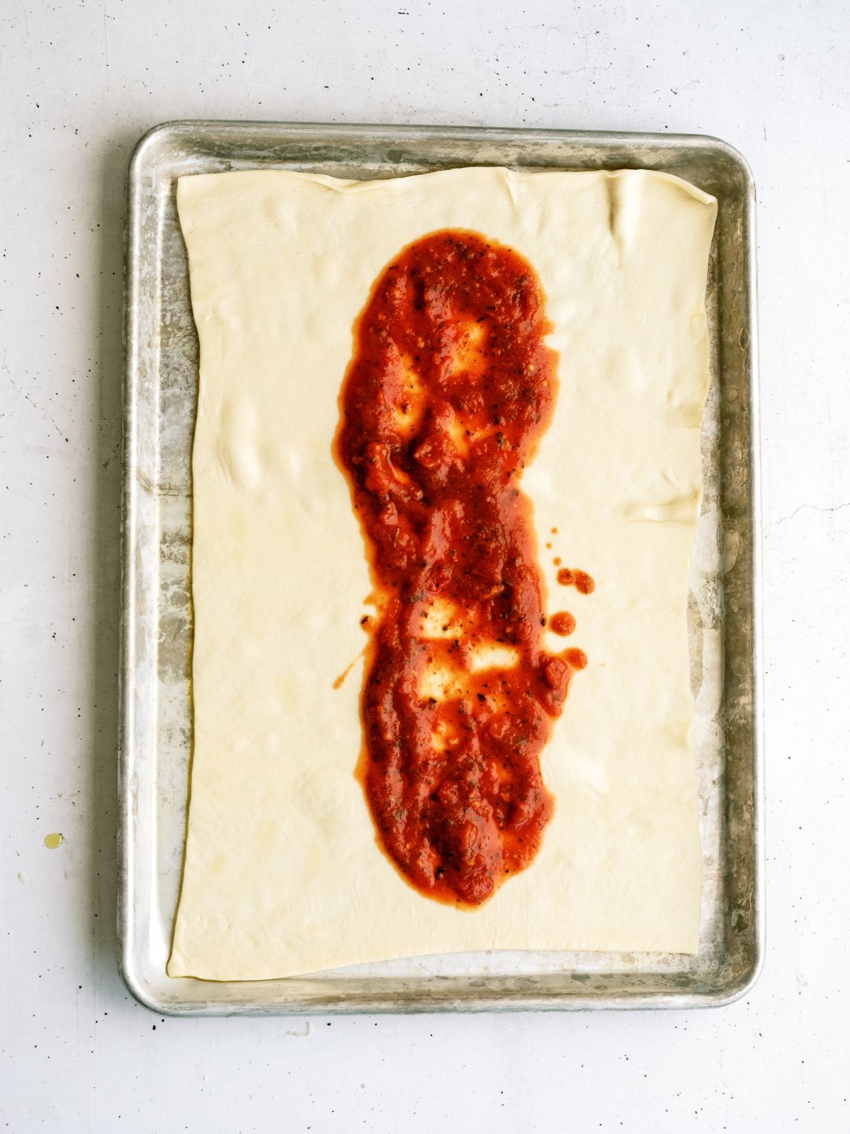 Pizza sauce down the center of the dough on a baking sheet