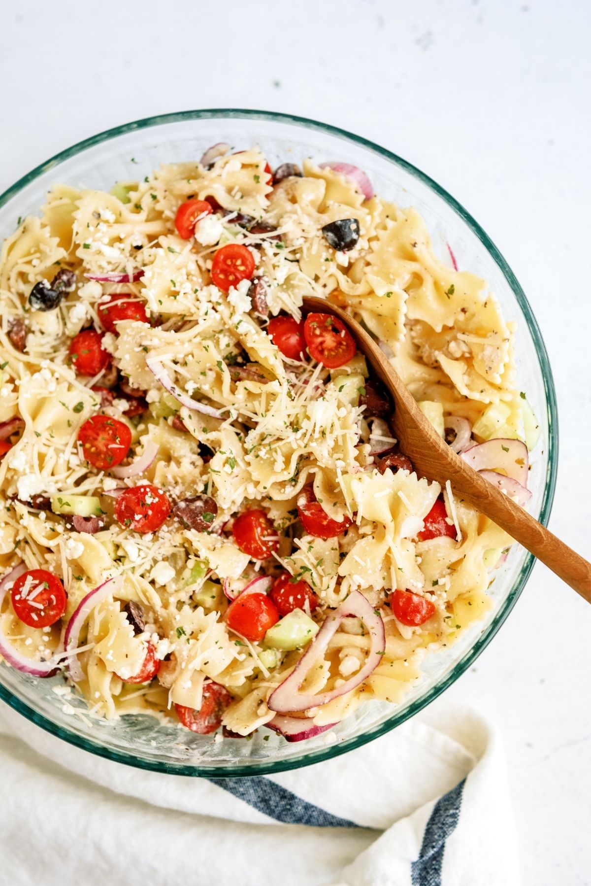 Greek Pasta Salad in a large glass bowl and wooden spoon