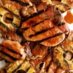 Grilled pork chops with char marks are served alongside grilled pineapple rings, all glazed with a brown sauce.