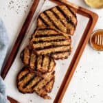 Four grilled pork chops with visible char marks arranged on a wooden tray, next to a small bowl of mustard and a dish with honey and a honey dipper.