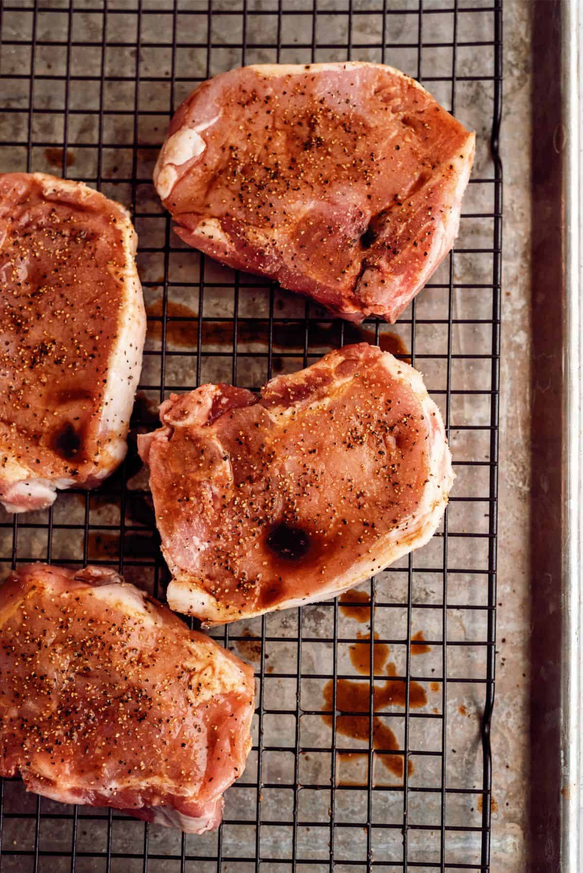 Seasoned pork chops sitting on cooling rack inside pan