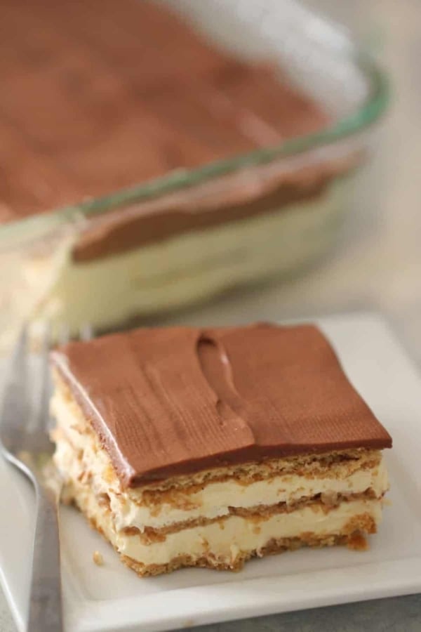 A slice of No Bake Eclair Cake on a plate with the rest of the cake in the background