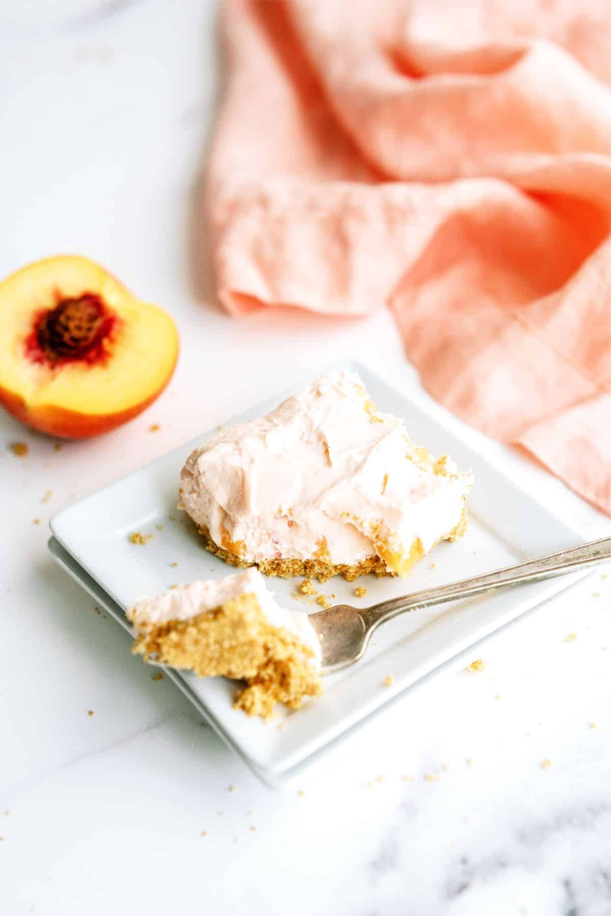 Slice of No-Bake Peach Cheesecake Bars on a plate with a fork taking a bite out of the bar