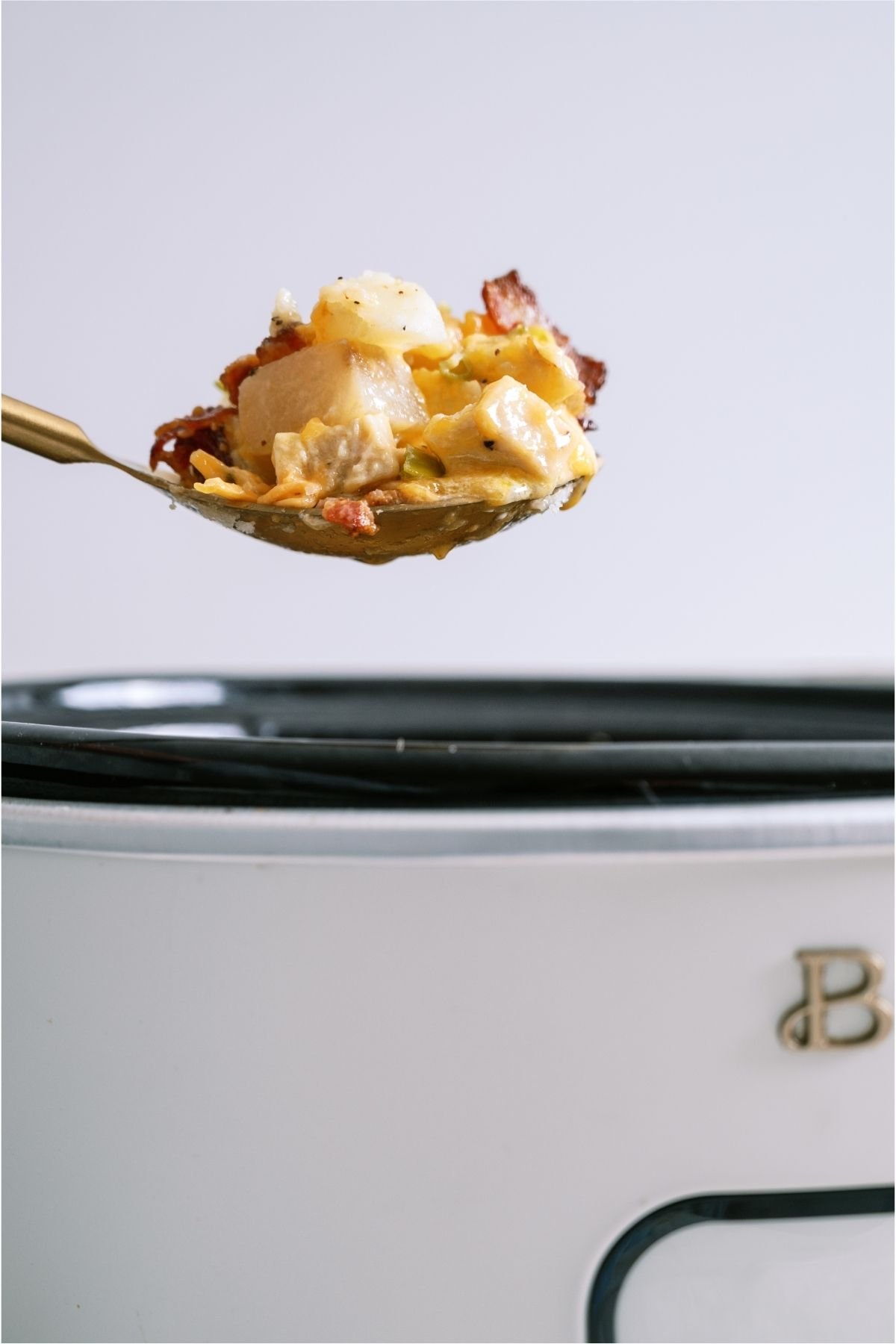A spoon lifting a scoop of Slow Cooker Loaded Chicken and Potato Casserole out of the slow cooker.