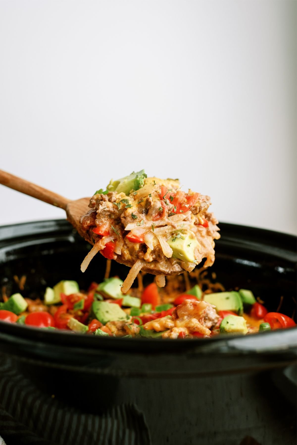 A spoon holding a scoop of Slow Cooker Mexican Hamburger Hashbrown Casserole above the slow cooker