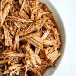 Shredded sweet pulled pork served in a white oval dish on a light-colored surface.