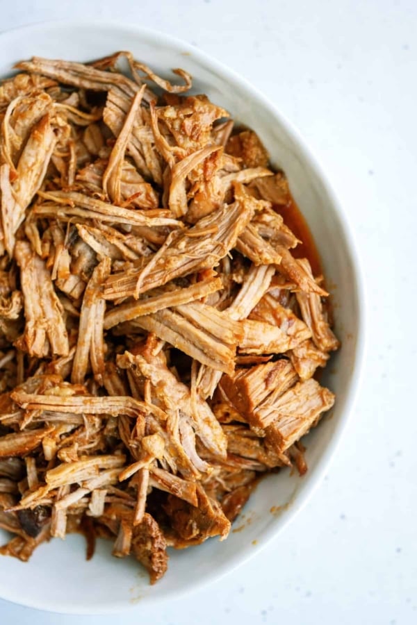 Shredded sweet pulled pork served in a white oval dish on a light-colored surface.
