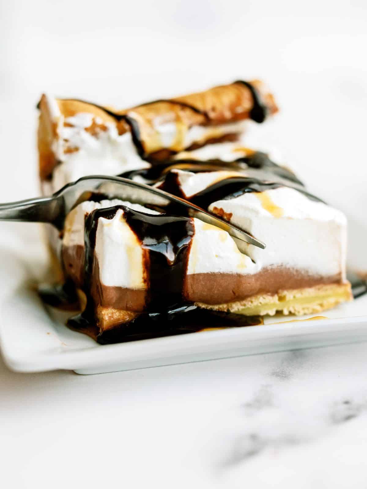 A fork slicing a bite of Cream Puff Cake Dessert of a slice on a dish.