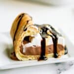 A slice of Cream Puff Cake Dessert drizzled with chocolate on a plate.