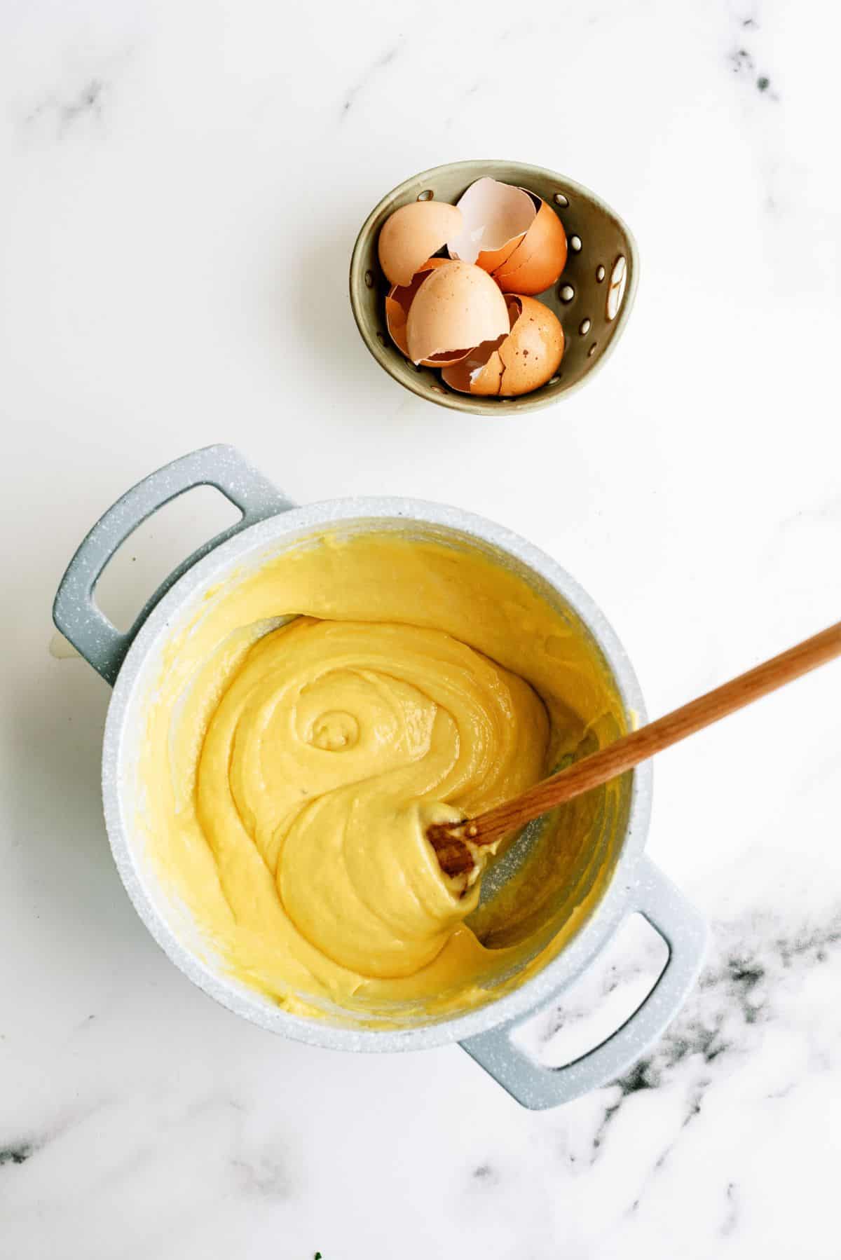 Cream Puff Cake dough in a mixing bowl with a wooden spoon.