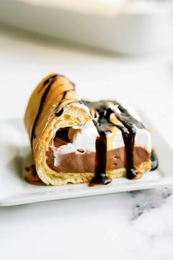 A slice of Cream Puff Cake Dessert drizzled with chocolate on a plate.