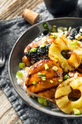 A bowl of grilled chicken topped with pineapple slices, green onions, and served over white rice.