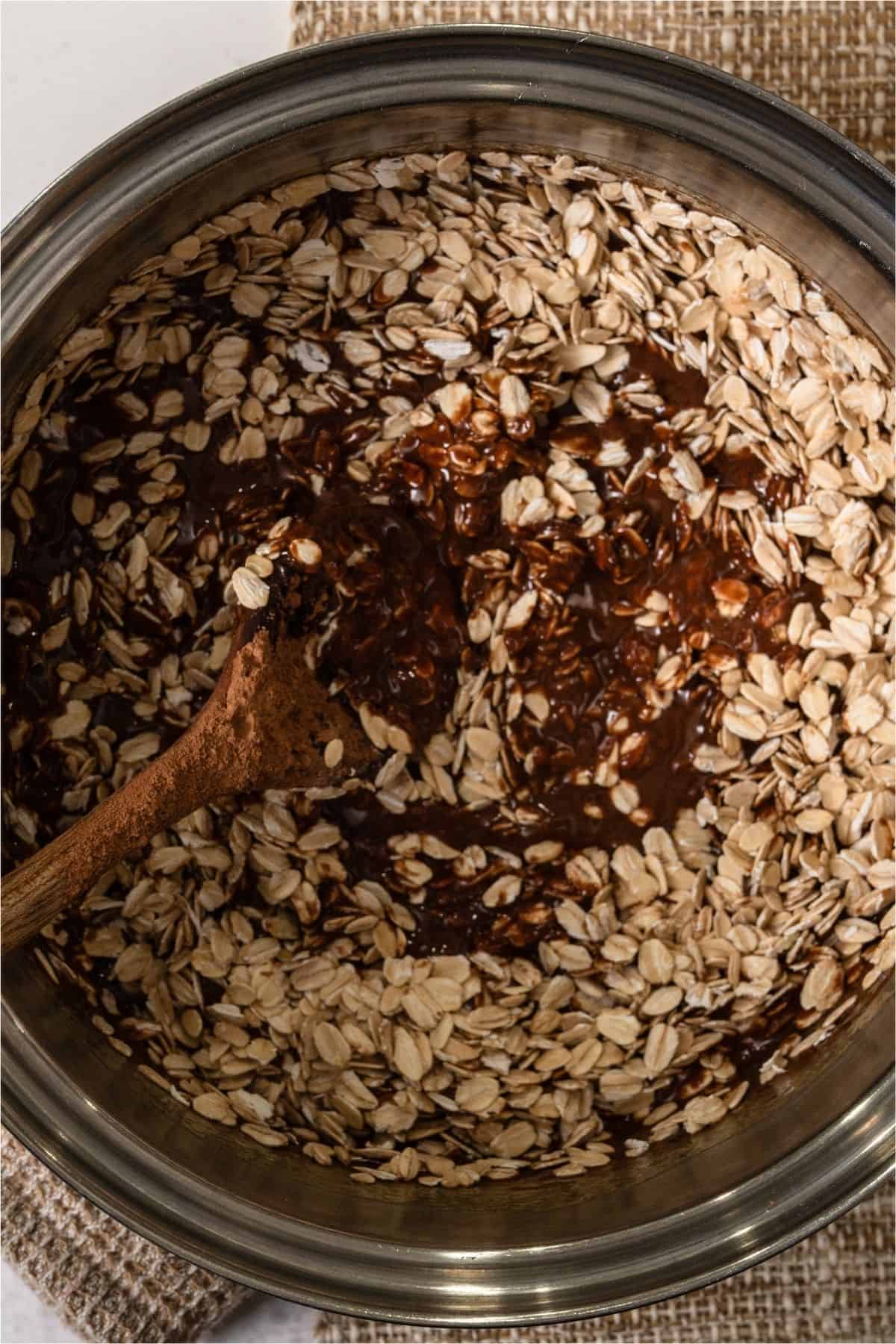 Adding oats to the chocolate peanut butter mixture in a sauce pan.