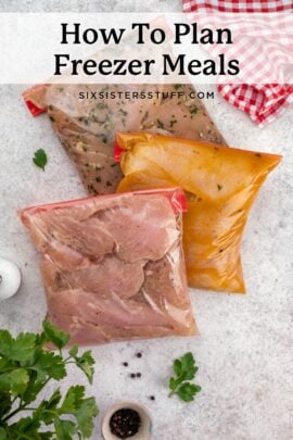 Three bags of prepared freezer meals lie on a countertop next to parsley, peppercorns, and a red-checkered cloth.