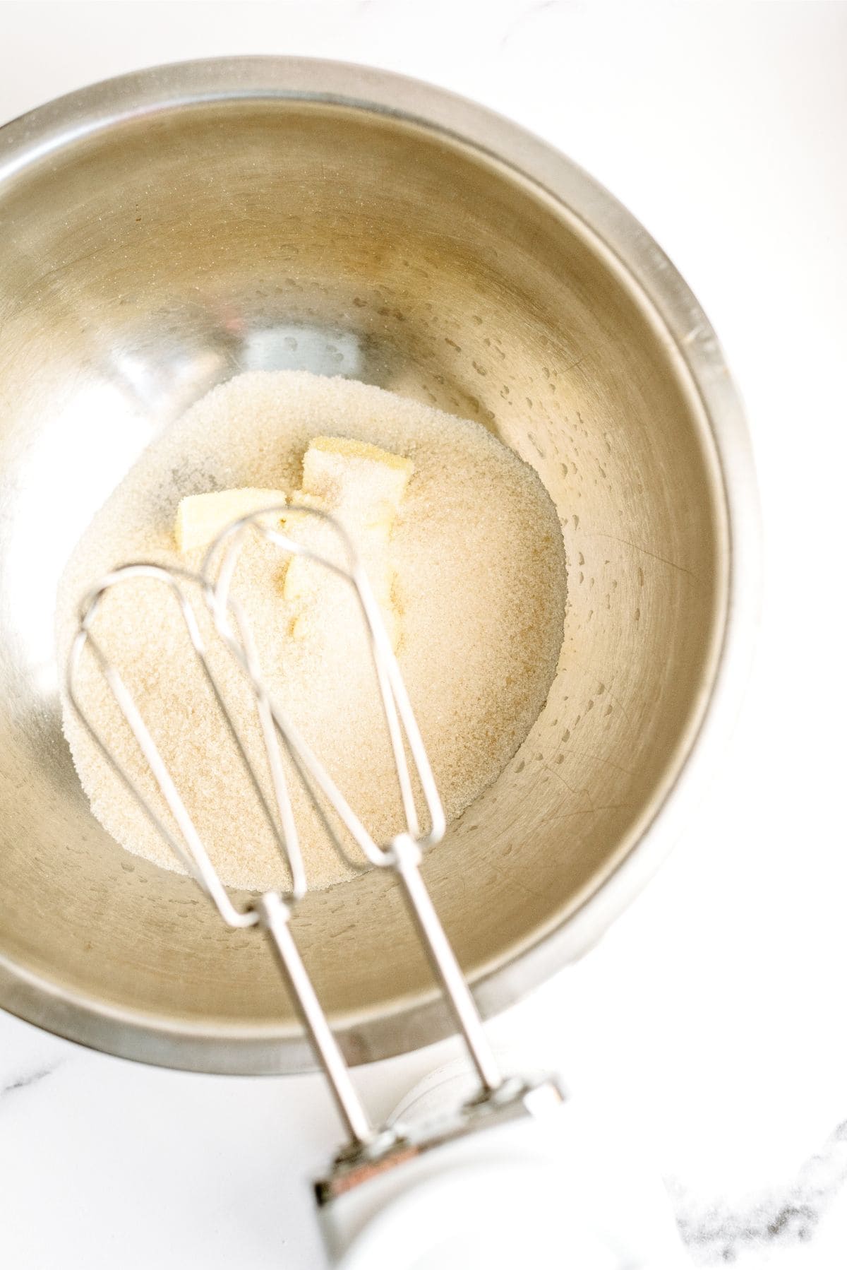 Sugar and butter mixed together in a bowl with a hand mixer