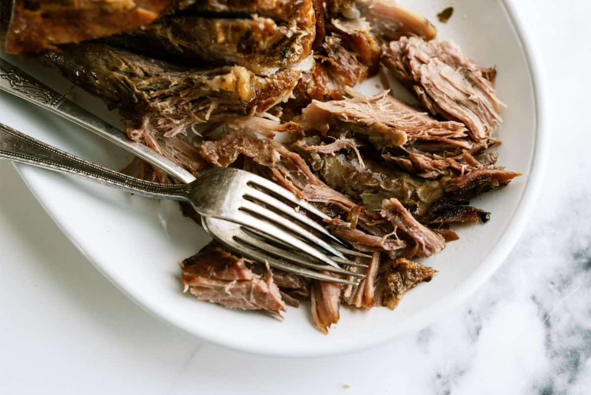 Oven Roasted Pork Shoulder shredded on a plate with 2 forks