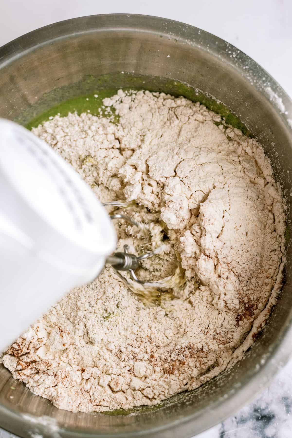 Mixing in dry ingredients into cake batter in mixing bowl with hand mixer.