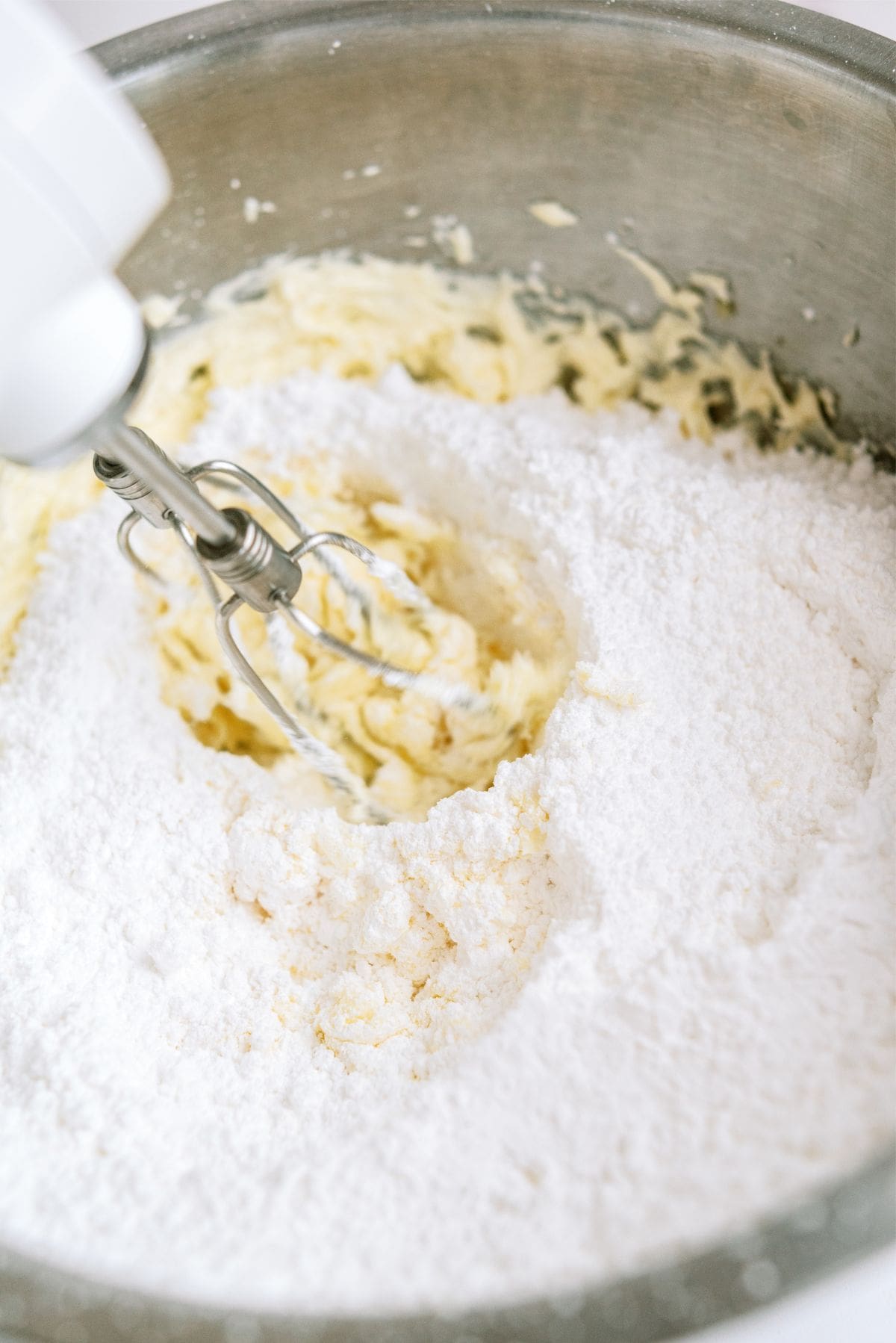 Mixing ingredients for frosting together with a hand mixer in a mixing bowl.