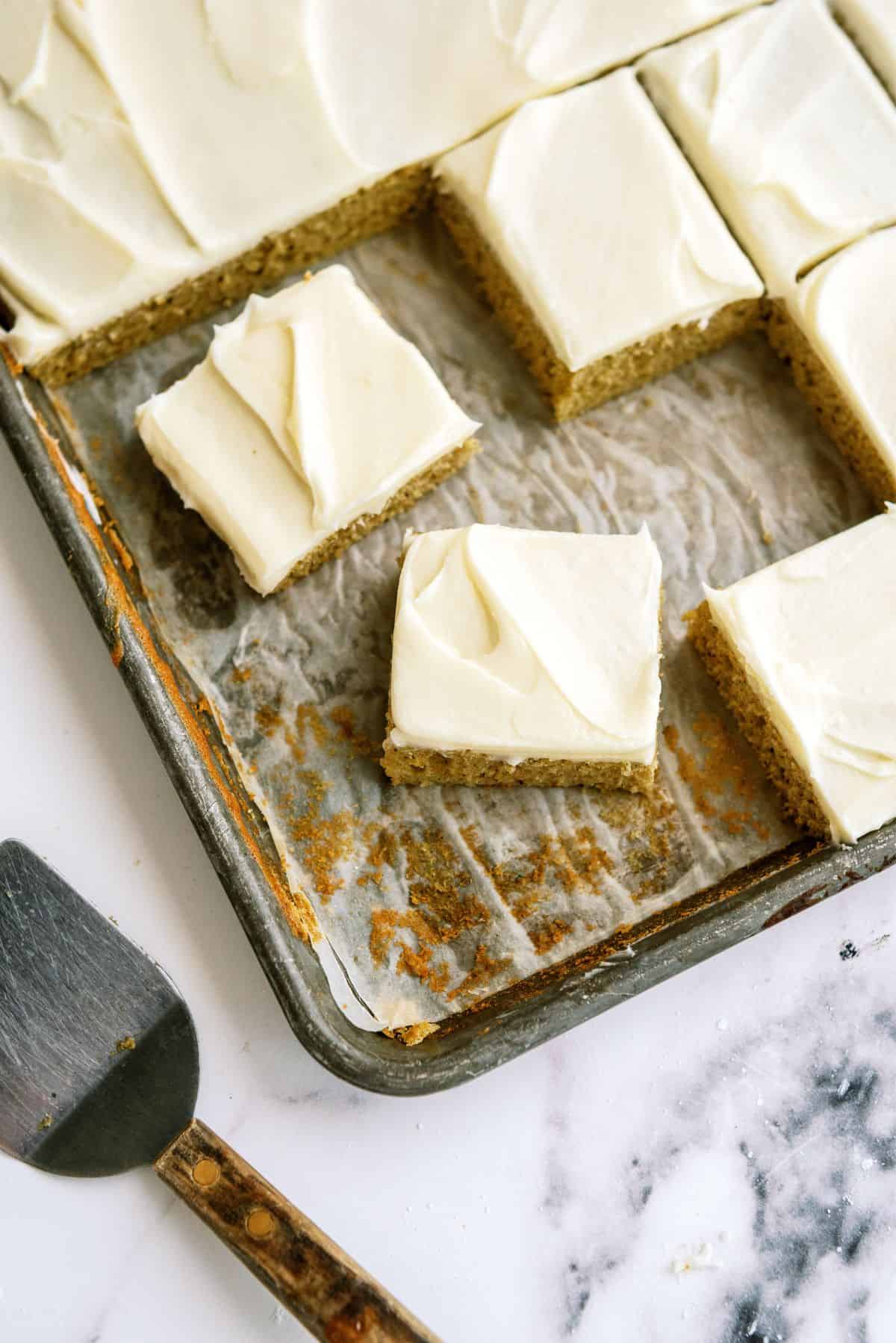 Sheet Pan Zucchini Cake with Frosting cut into squares on a baking sheet.