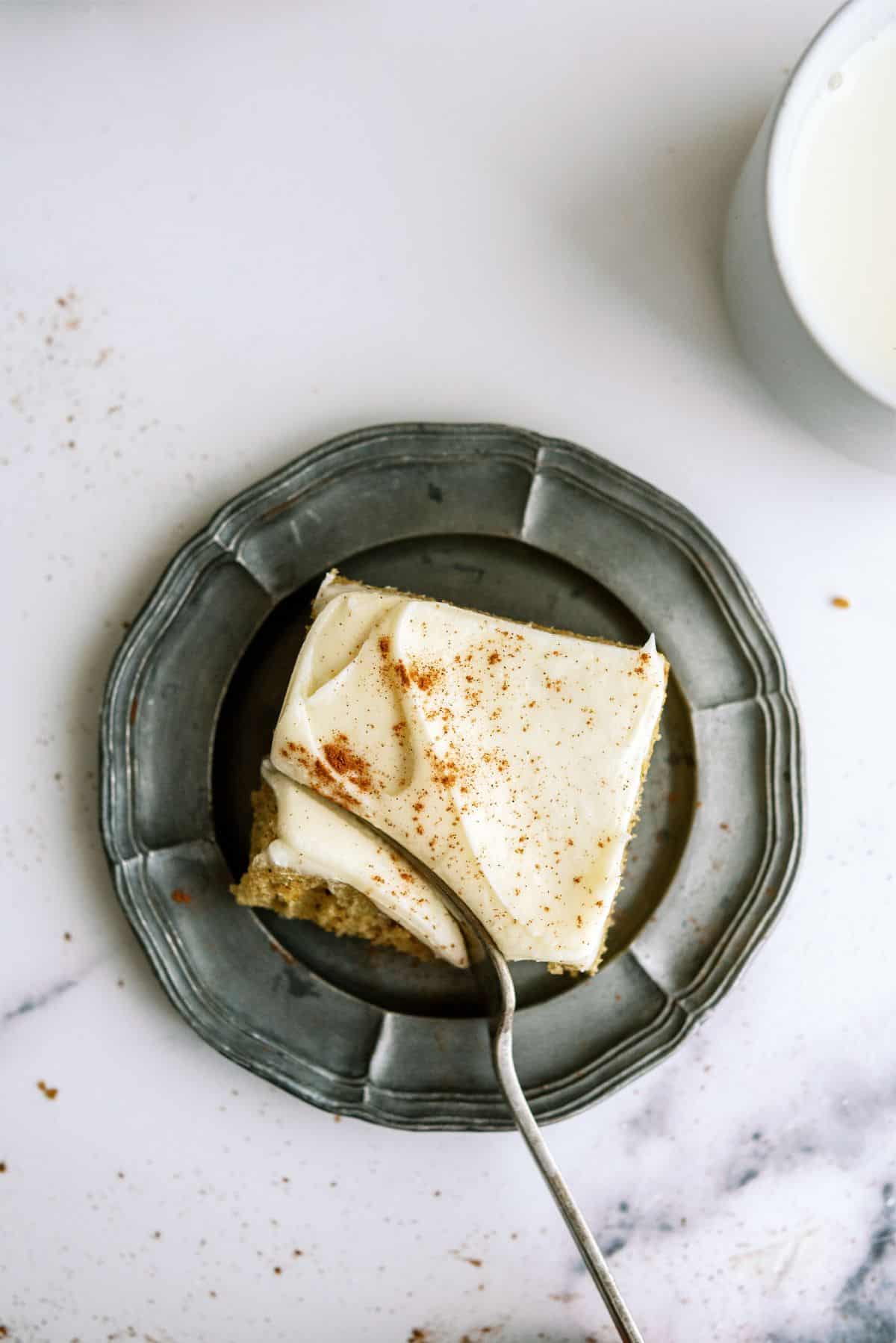 A fork slicing a bite of a slice of Sheet Pan Zucchini Cake with Frosting on a plate.