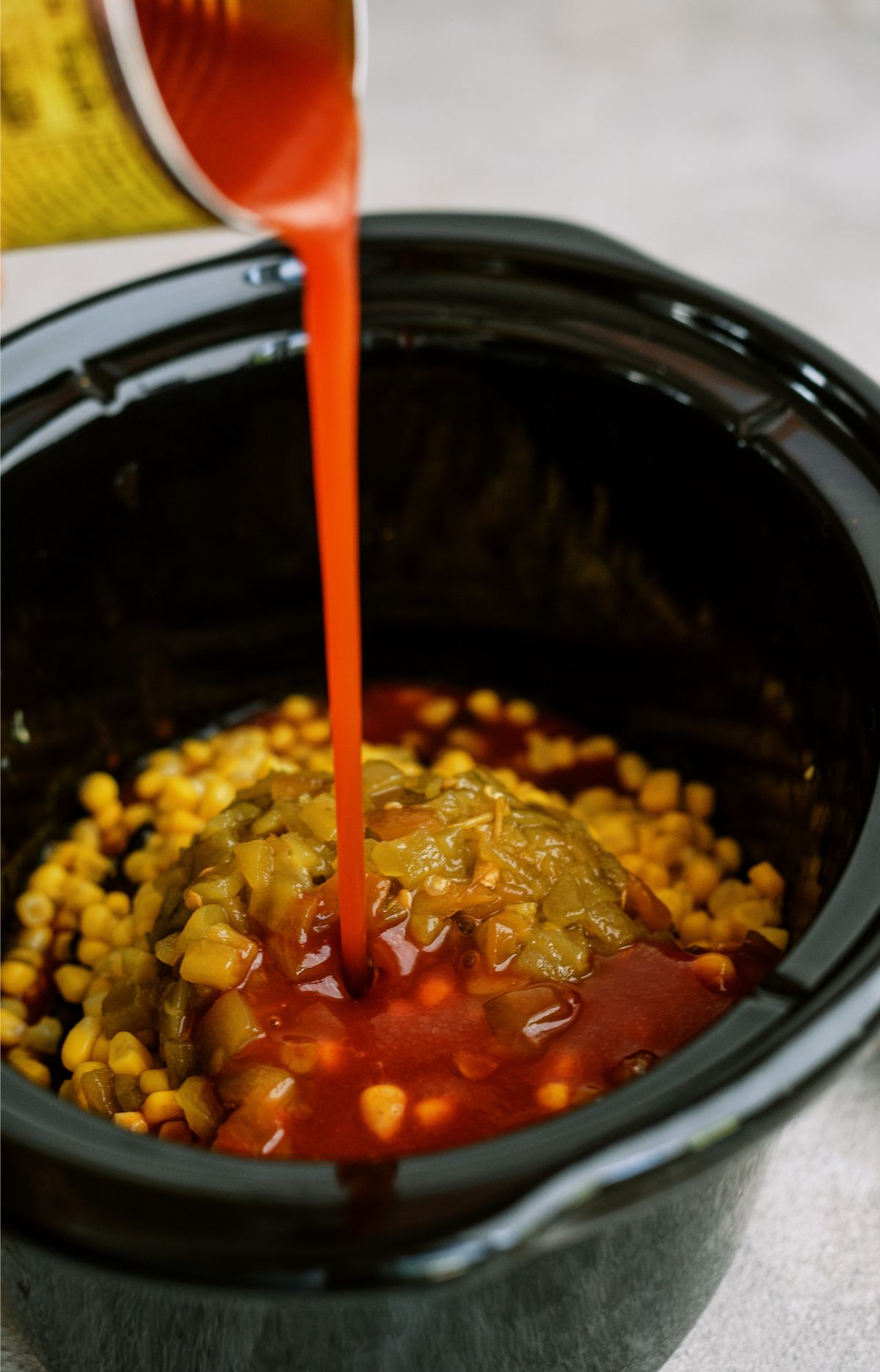 Pouring enchilada sauce on top of ingredients in slow cooker