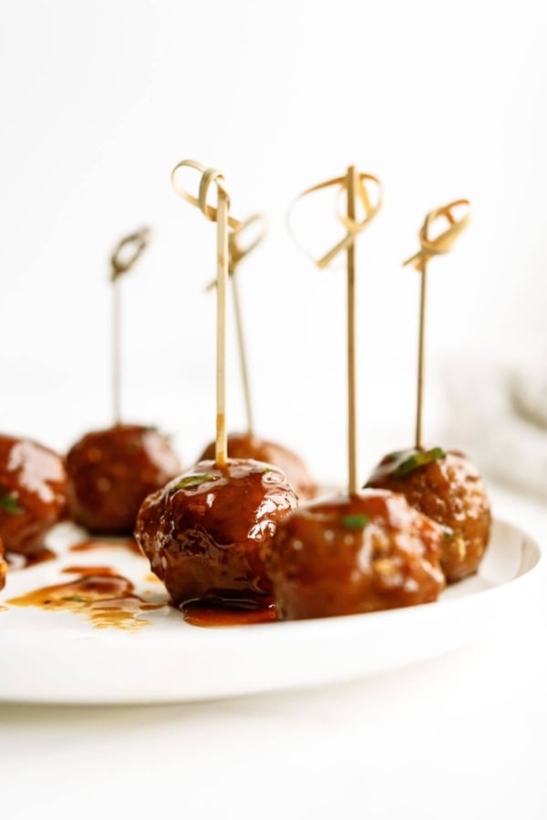Meatballs glazed with sauce, each skewered with a decorative toothpick, are arranged on a white plate.