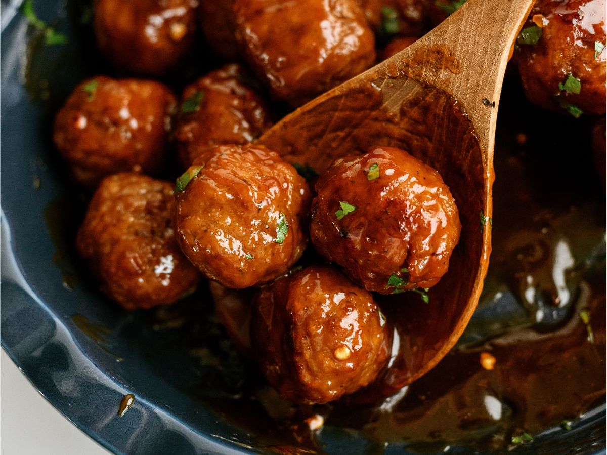 Slow Cooker Honey Buffalo Meatballs in a serving dish with a wooden spoon lifting 3 meatballs out