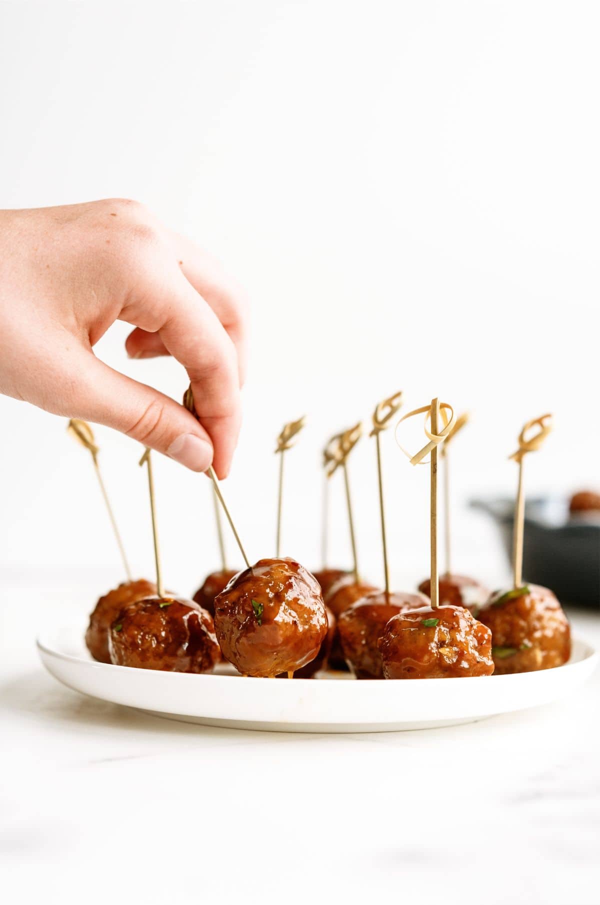 Slow Cooker Honey Buffalo Meatballs on a serving plate with toothpicks. A hand picking up one of the meatballs